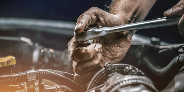 A mechanic works on a car engine with a wrench, representing the trades and service businesses that access CADDA small business loans.