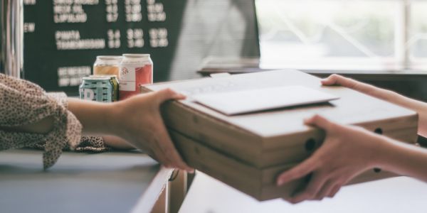 A small business employee hands pizza boxes to a customer at a counter, illustrating the local retail and hospitality businesses CADDA helps fund.